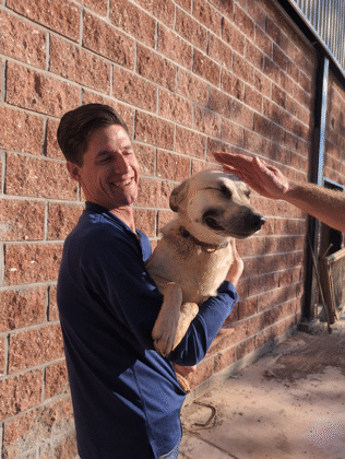 Man holding and petting happy dog outside.