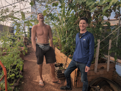 Two men smiling in a greenhouse garden.